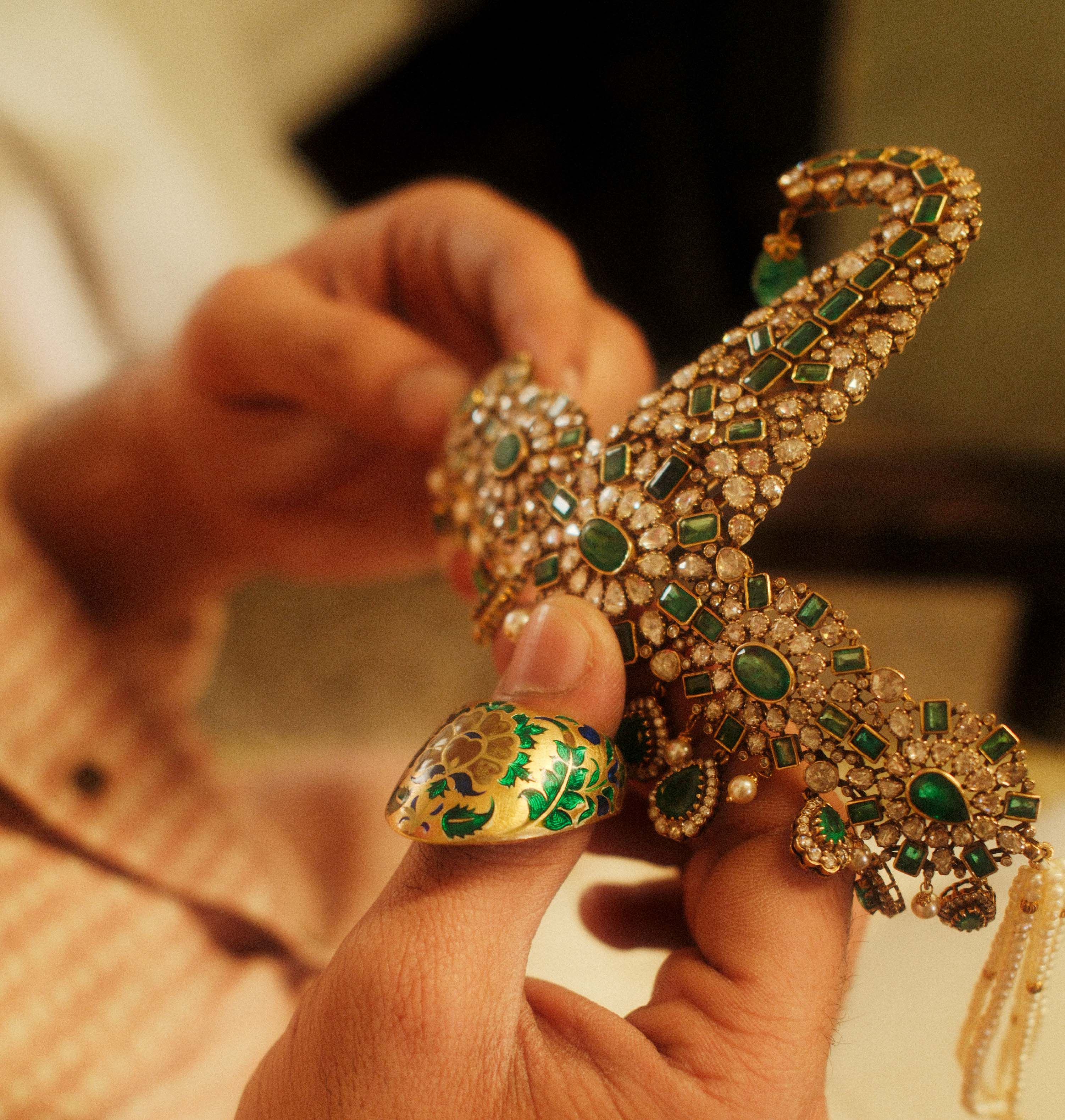 Hands holding an emerald and polki sarpech, a meenakari ring on the thumb